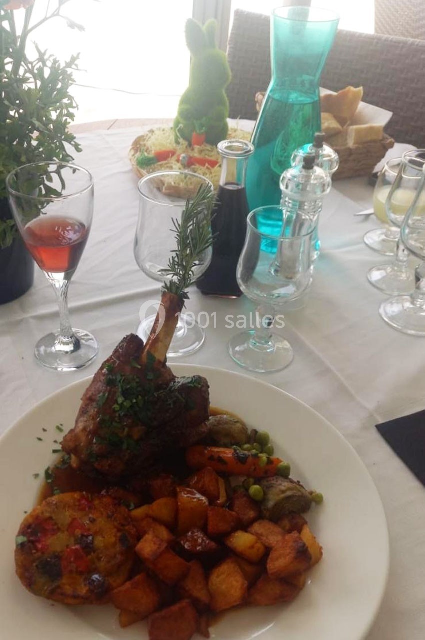 Assiette garnie d'un jarret d'agneau, légumes, pommes de terre rôties, sur une table dressée avec boissons et décorations.