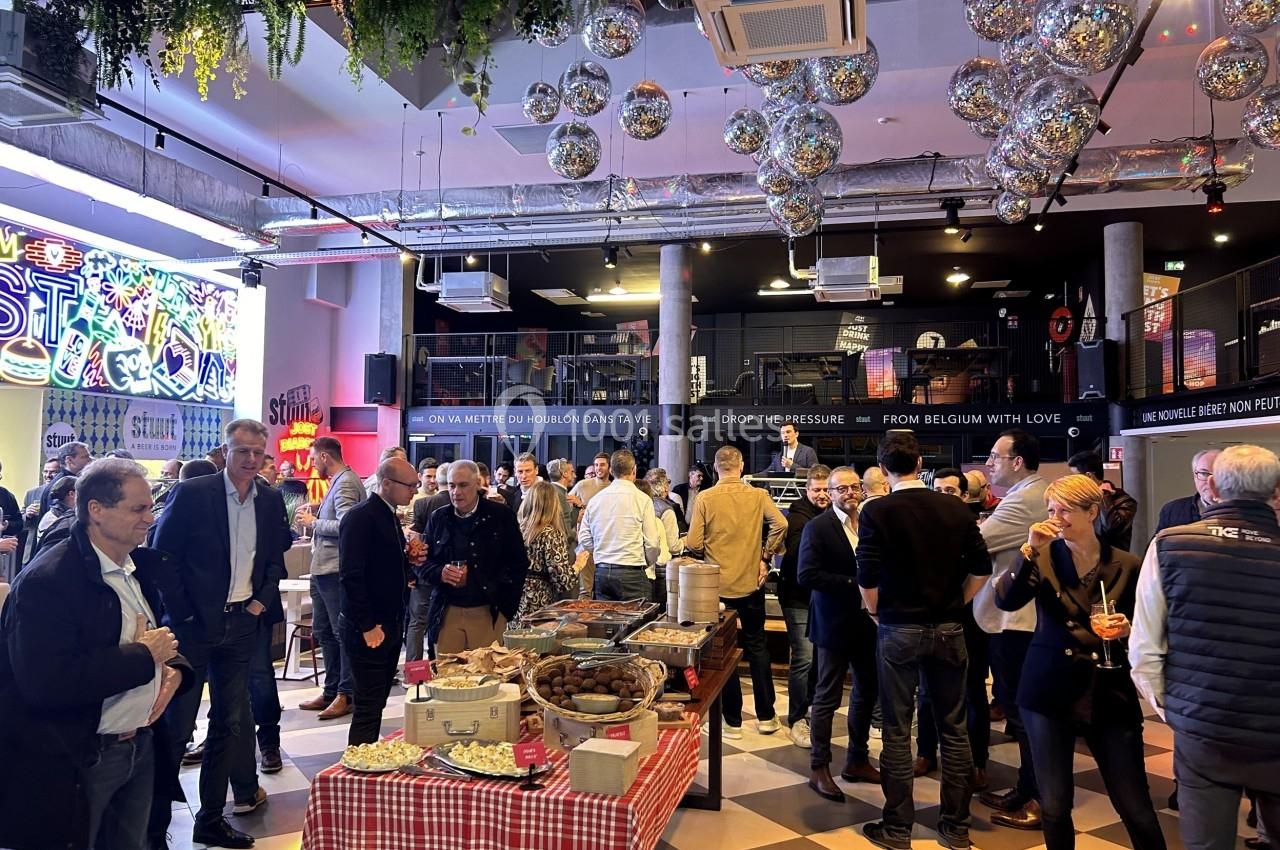 Groupe de personnes échangeant dans un espace intérieur décoré avec des guirlandes lumineuses et des tables de buffet.