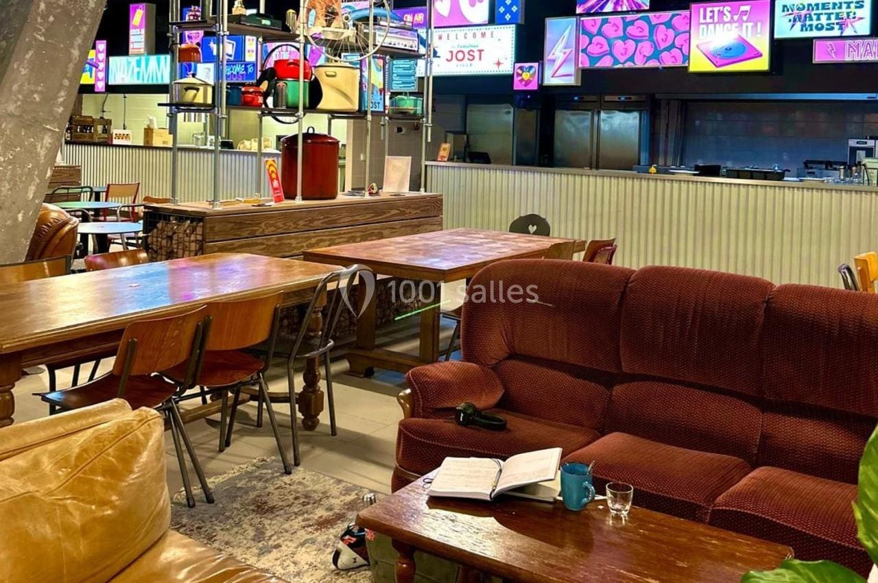 Espace intérieur avec tables en bois, fauteuils, carnet ouvert et écrans colorés affichant des visuels lumineux en arrière…