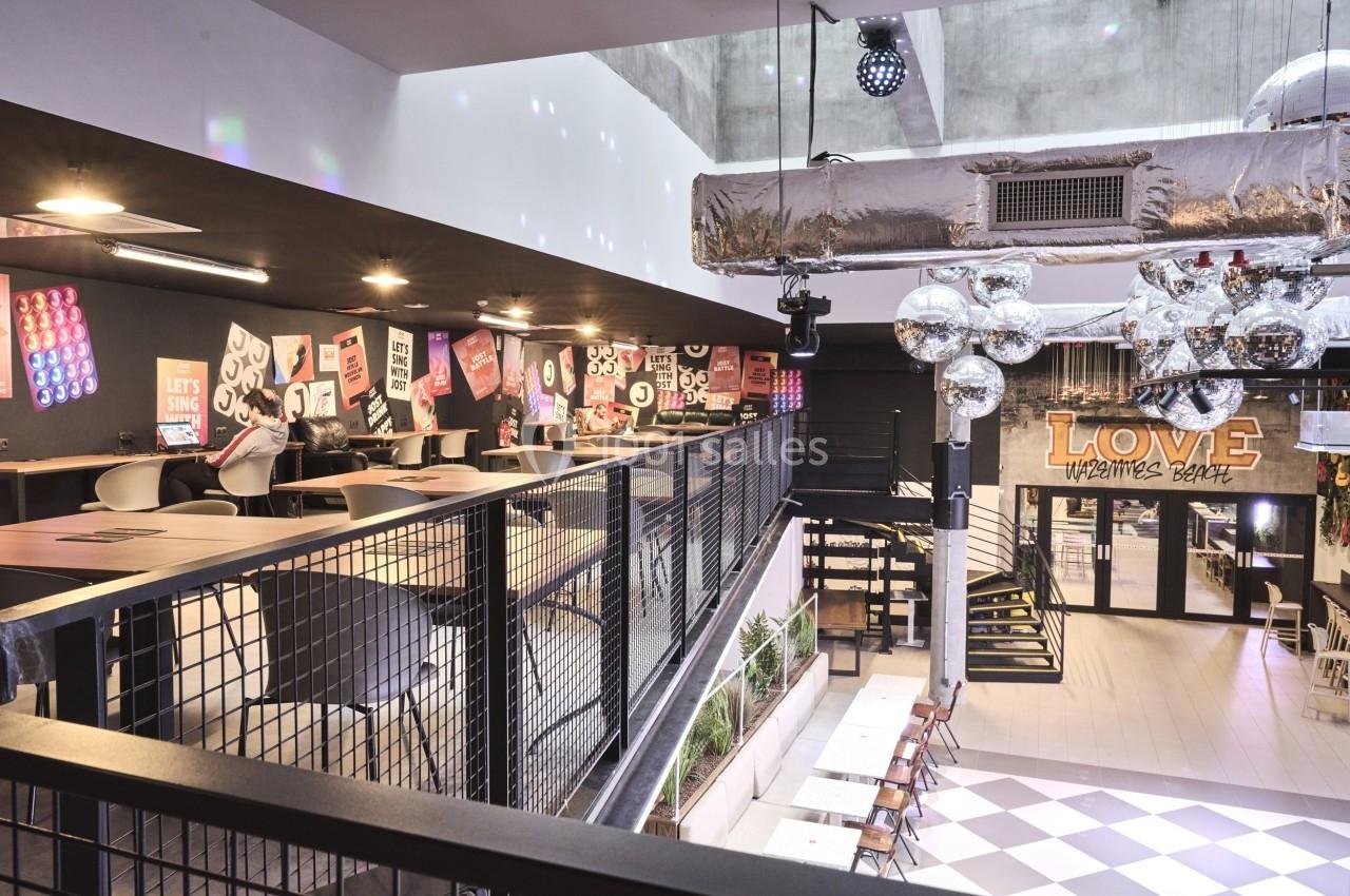 Intérieur d'un restaurant moderne avec mezzanine, tables alignées, décorations murales et luminaires suspendus.