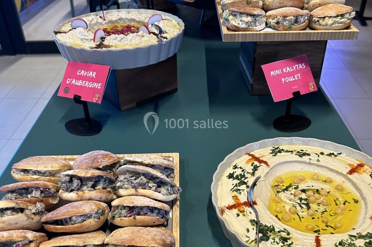 Plateau de mini sandwichs garnis et plats de mezzés, dont du caviar d’aubergine et du houmous, sur une table verte.