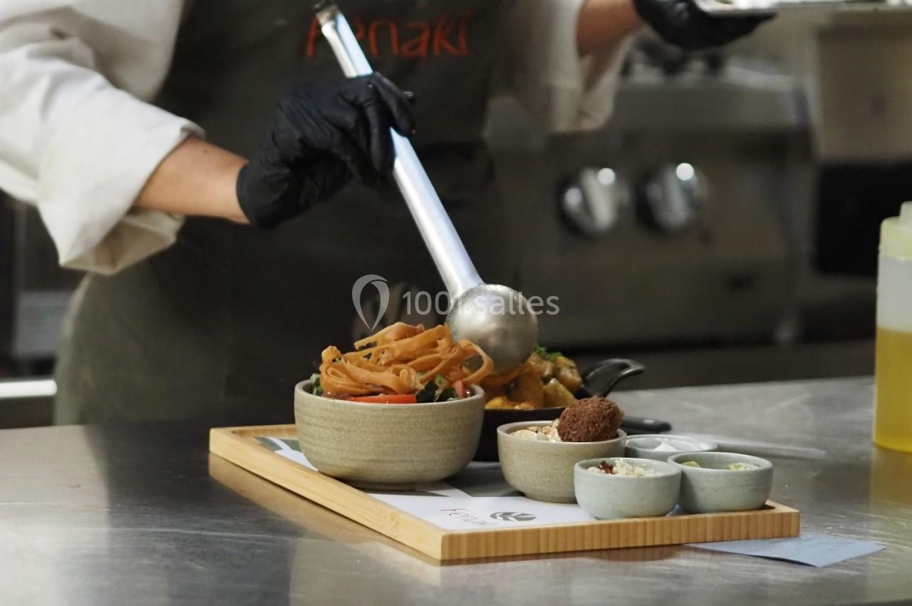 Un cuisinier sert des nouilles dans un bol avec une louche, accompagné de petites portions d'accompagnements.