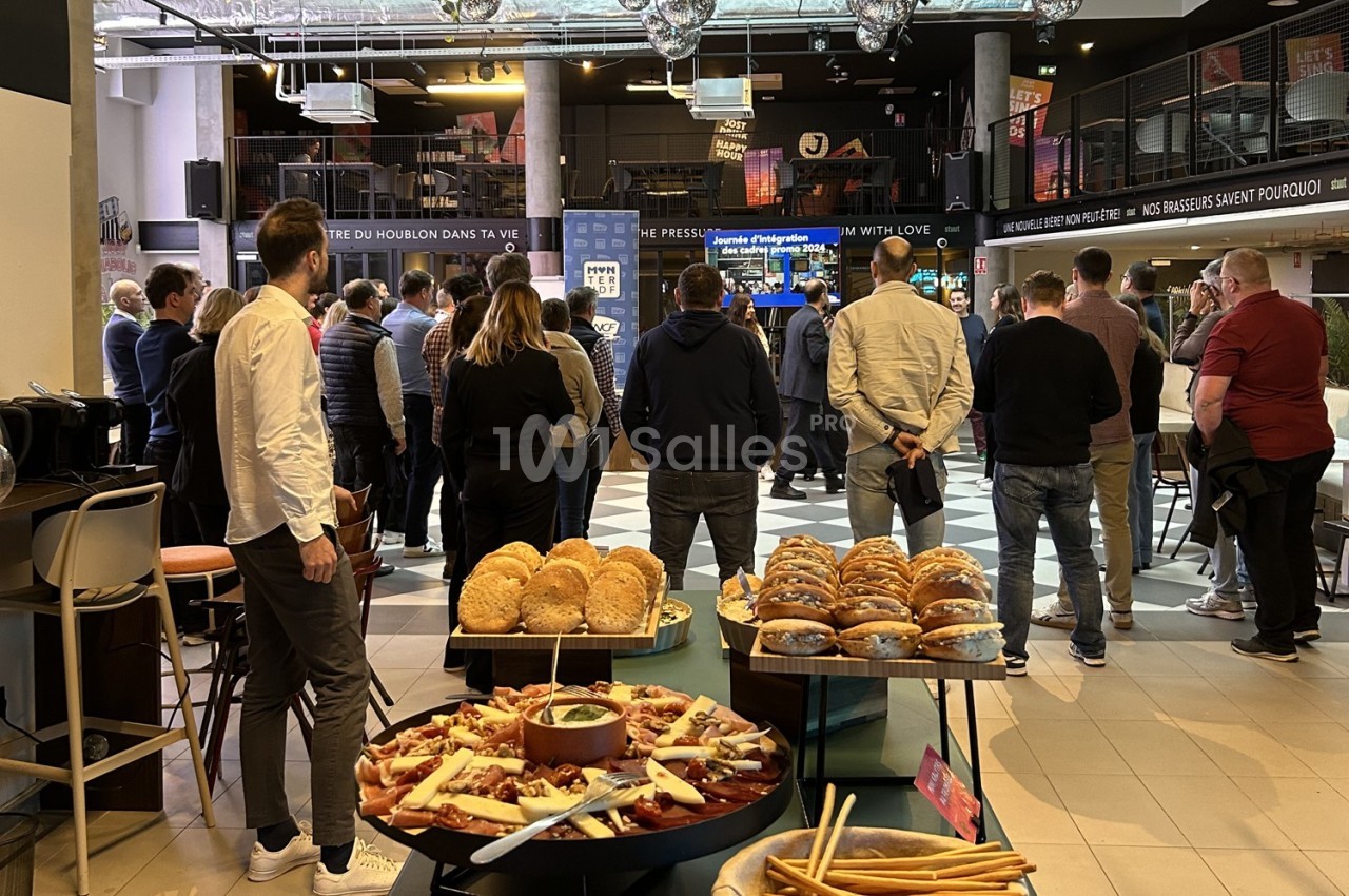 Groupe de personnes debout dans un espace intérieur, avec des tables garnies de snacks et de pains au premier plan.