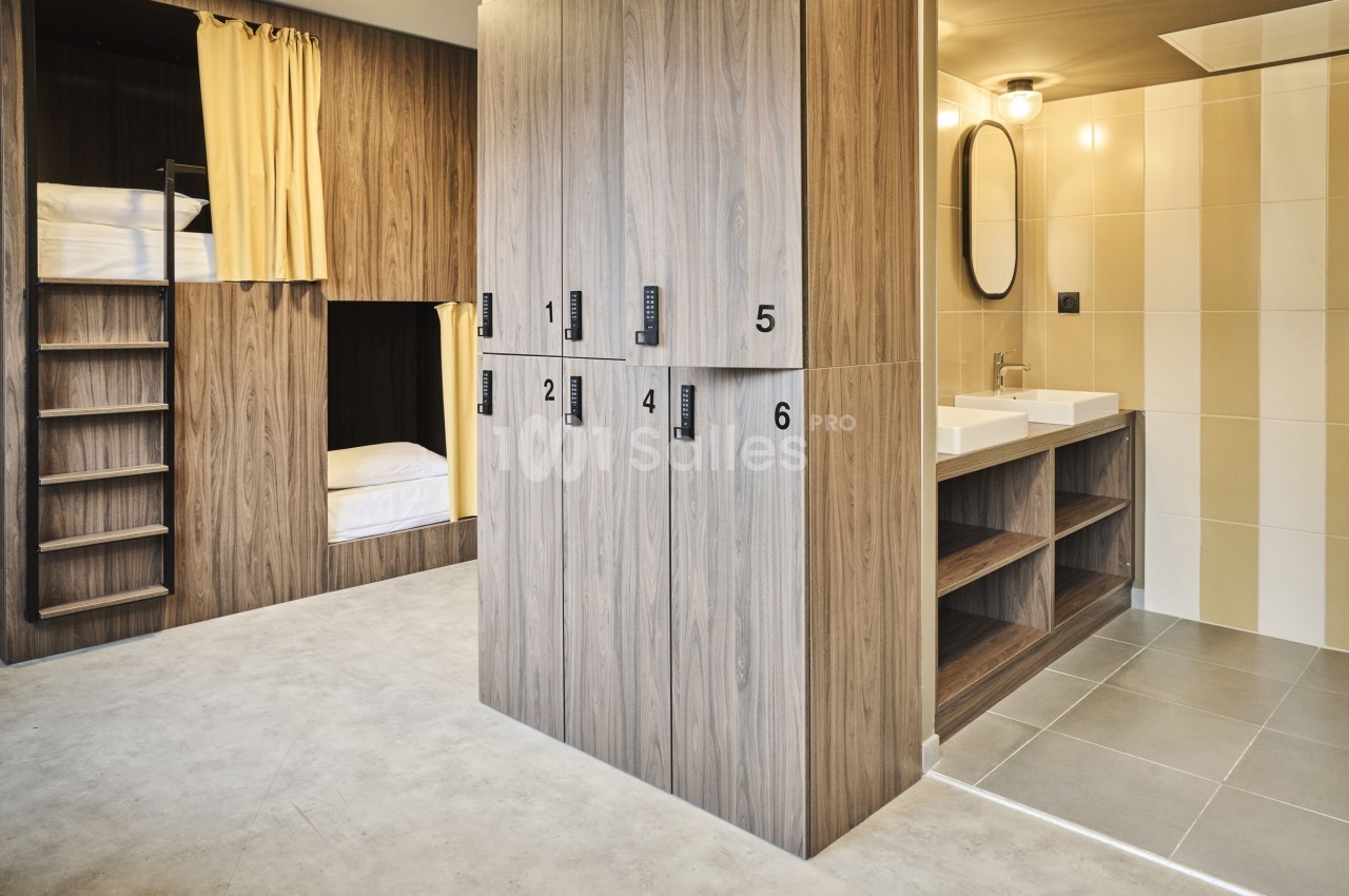 Dortoir moderne avec lits superposés, casiers en bois numérotés et salle de bain attenante équipée de lavabos.