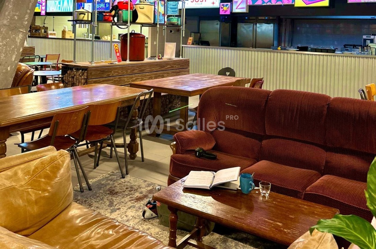 Espace intérieur avec canapés, tables en bois, livre ouvert et tasse sur une table basse, ambiance décontractée.
