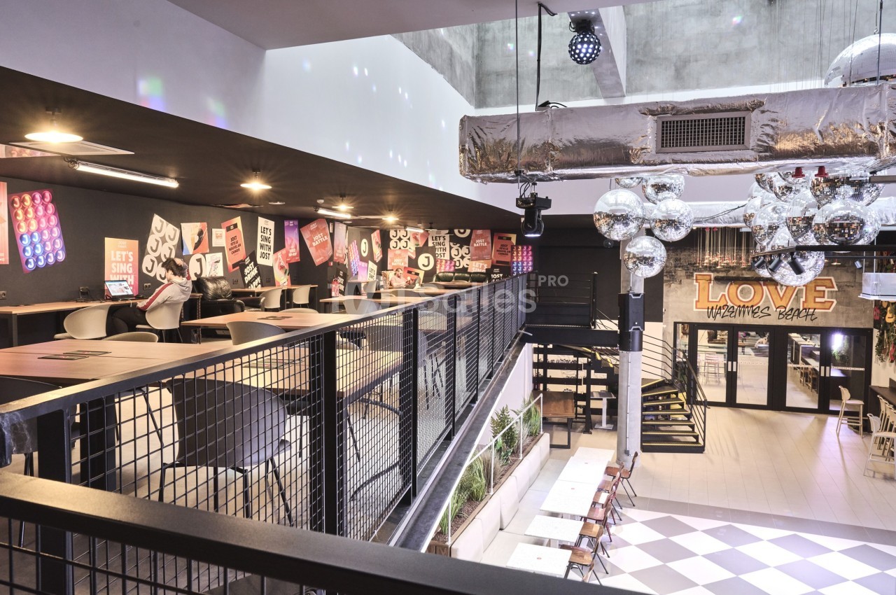 Intérieur d'un restaurant moderne avec mezzanine, tables alignées, décorations murales et luminaires suspendus.