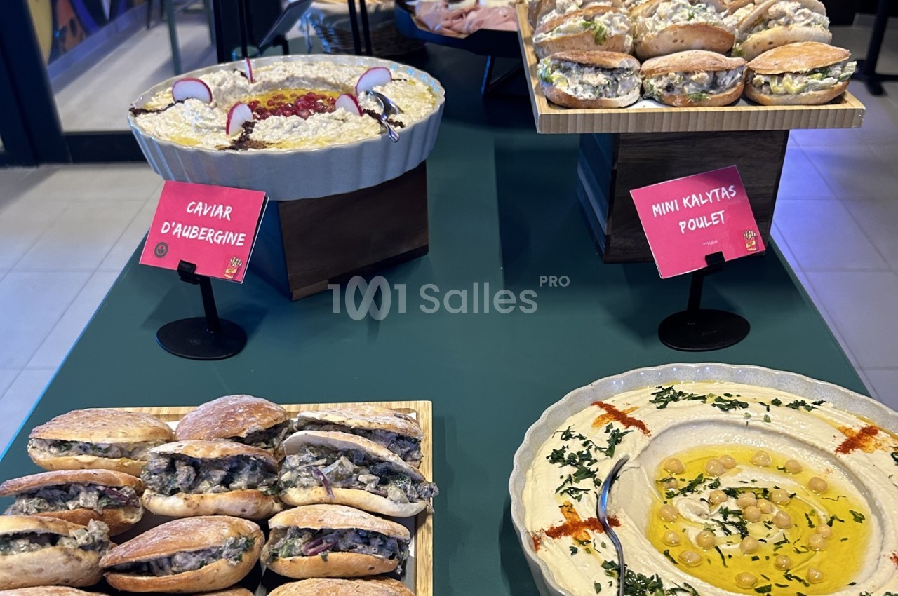 Plateau de mini sandwichs, caviar d’aubergine et houmous décoré, présentés sur une table verte.