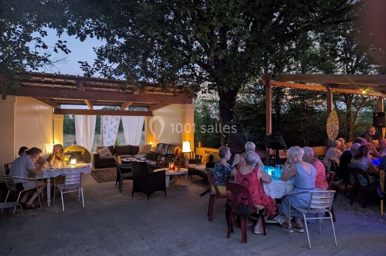 Des personnes dînent et discutent sous un abri extérieur éclairé, entouré d'arbres, en soirée.