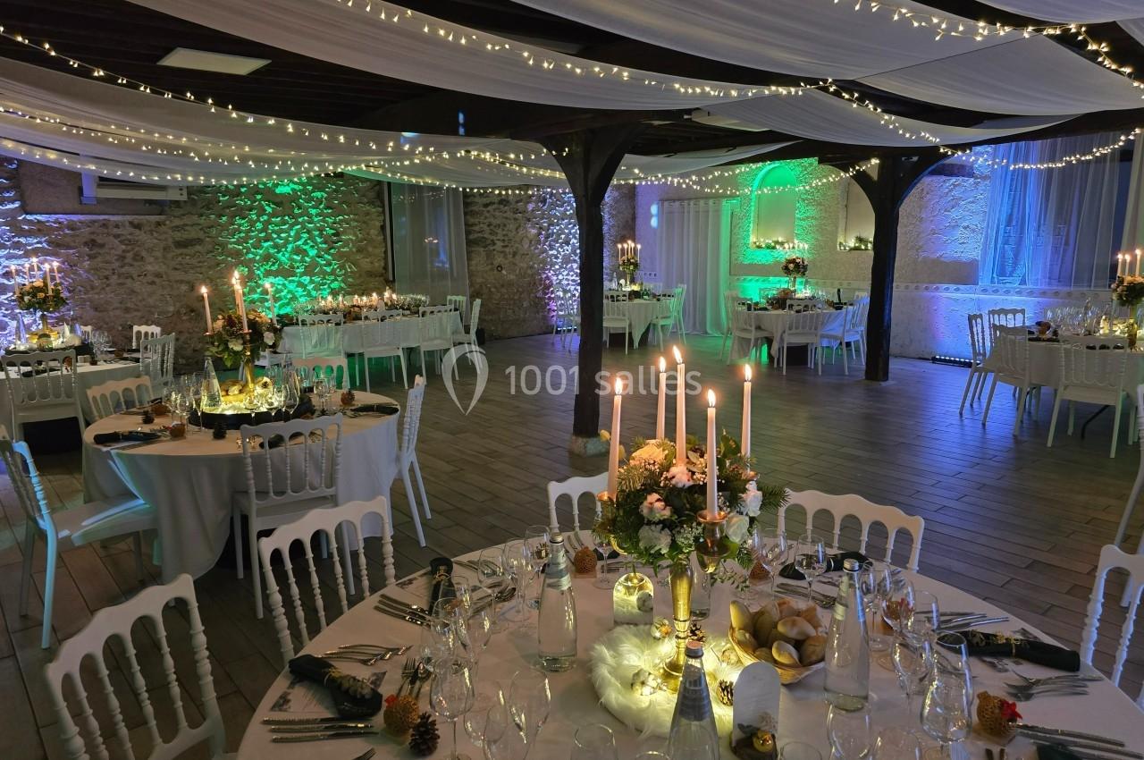 Salle de réception décorée avec des guirlandes lumineuses, tables dressées et éclairage d’ambiance coloré.