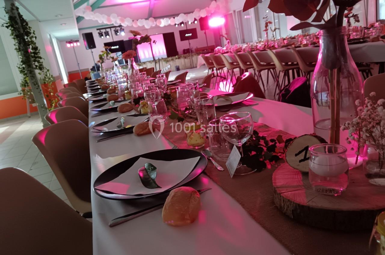 Table de réception décorée avec vaisselle, fleurs, bougies et lumière rose en arrière-plan.