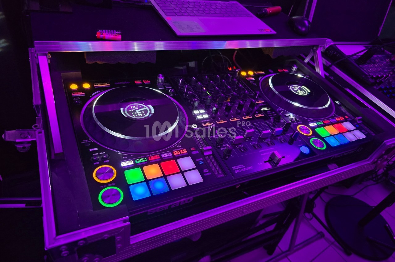Table de mixage DJ éclairée avec des boutons colorés, deux platines et un ordinateur portable en arrière-plan.