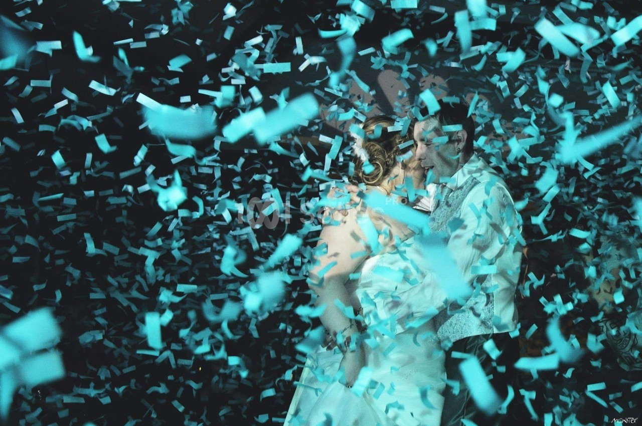 Un couple danse entouré de confettis bleus dans une ambiance festive et lumineuse.