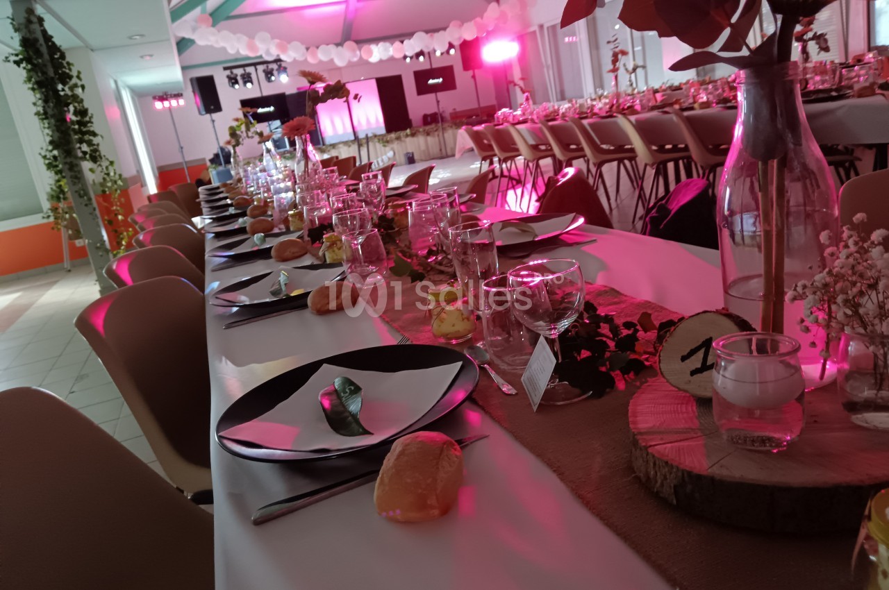 Table de réception décorée avec vaisselle, fleurs, bougies et lumière rose en arrière-plan.