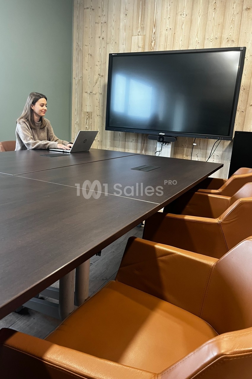 Une femme travaille sur un ordinateur portable dans une salle de réunion avec une grande table, des chaises en cuir et un…
