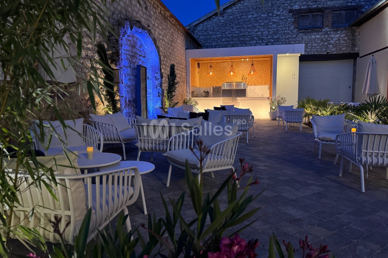 Terrasse extérieure en soirée avec mobilier moderne, éclairage chaleureux et mur en pierre en arrière-plan.
