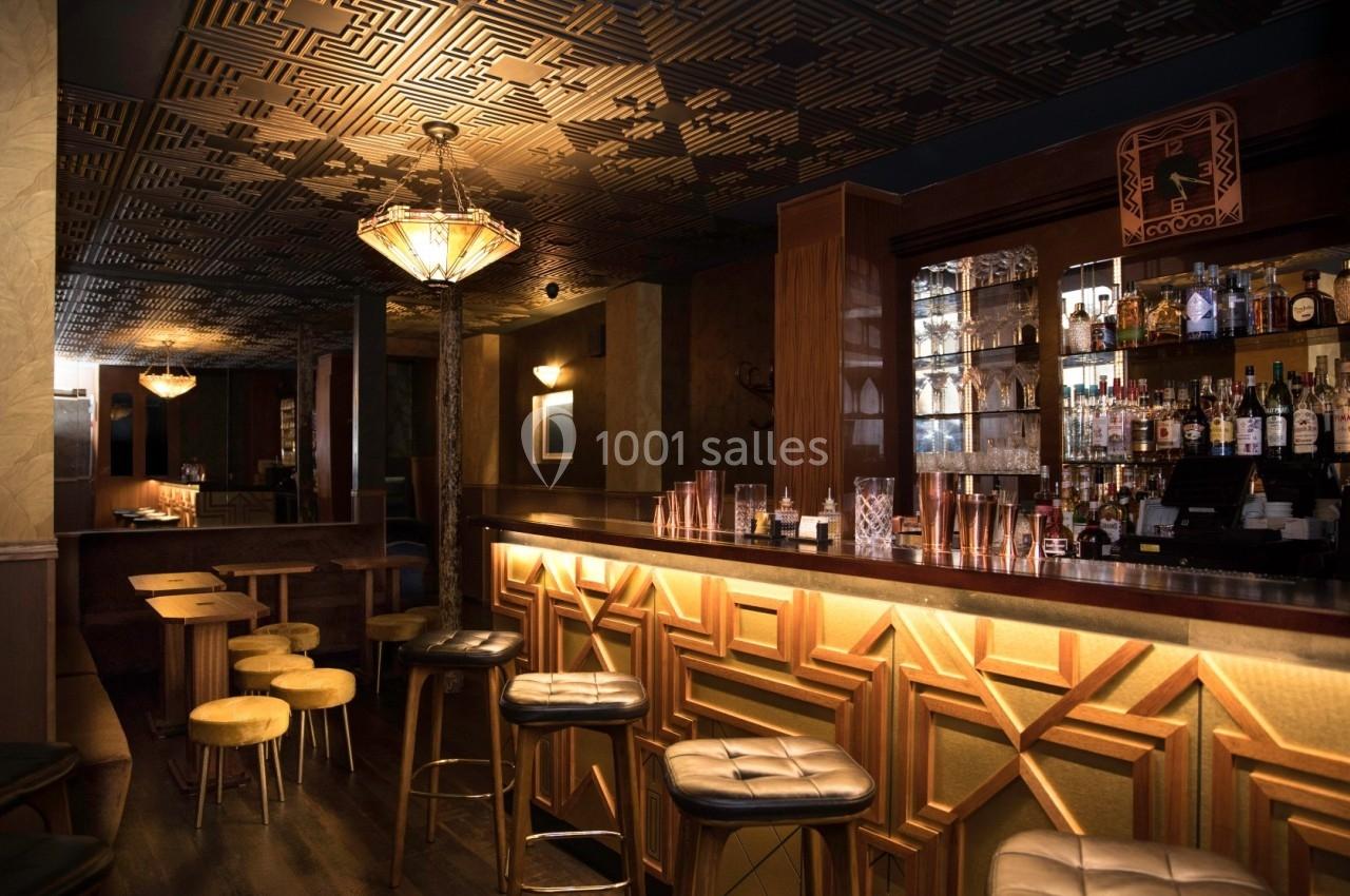 Bar élégant avec comptoir en bois, tabourets rembourrés, étagères de bouteilles et éclairage tamisé.