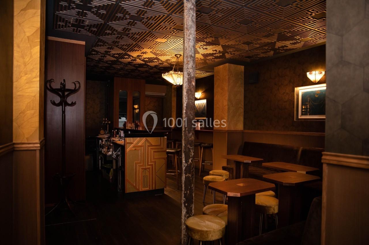 Intérieur d'un bar avec tables en bois, tabourets rembourrés, éclairage tamisé et décorations géométriques au plafond.