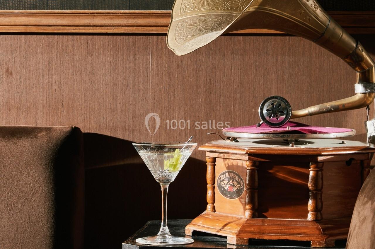 Un gramophone ancien en bois à côté d'un verre à cocktail sur une table sombre.