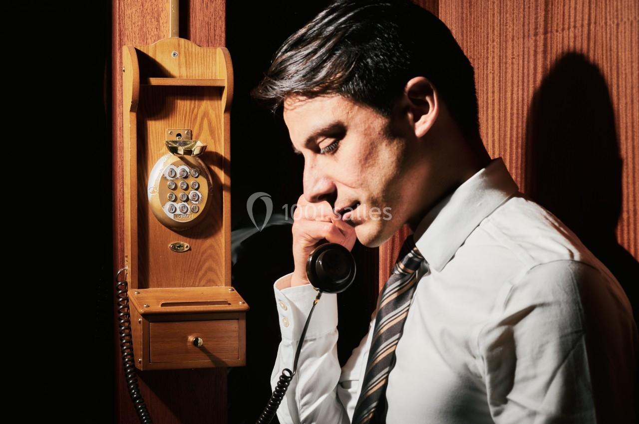 Un homme en chemise blanche utilise un téléphone fixe en bois dans un environnement sombre.