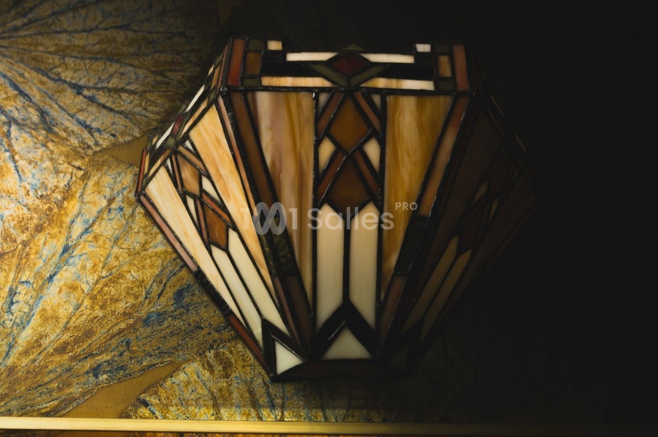 Lampe en vitrail coloré de style art déco, posée sur une surface texturée aux tons dorés et bleus.