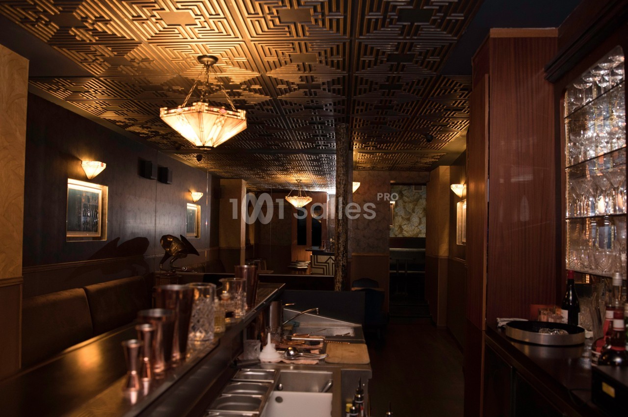 Intérieur d'un bar élégant avec un comptoir en premier plan, un plafond décoratif et un éclairage tamisé.