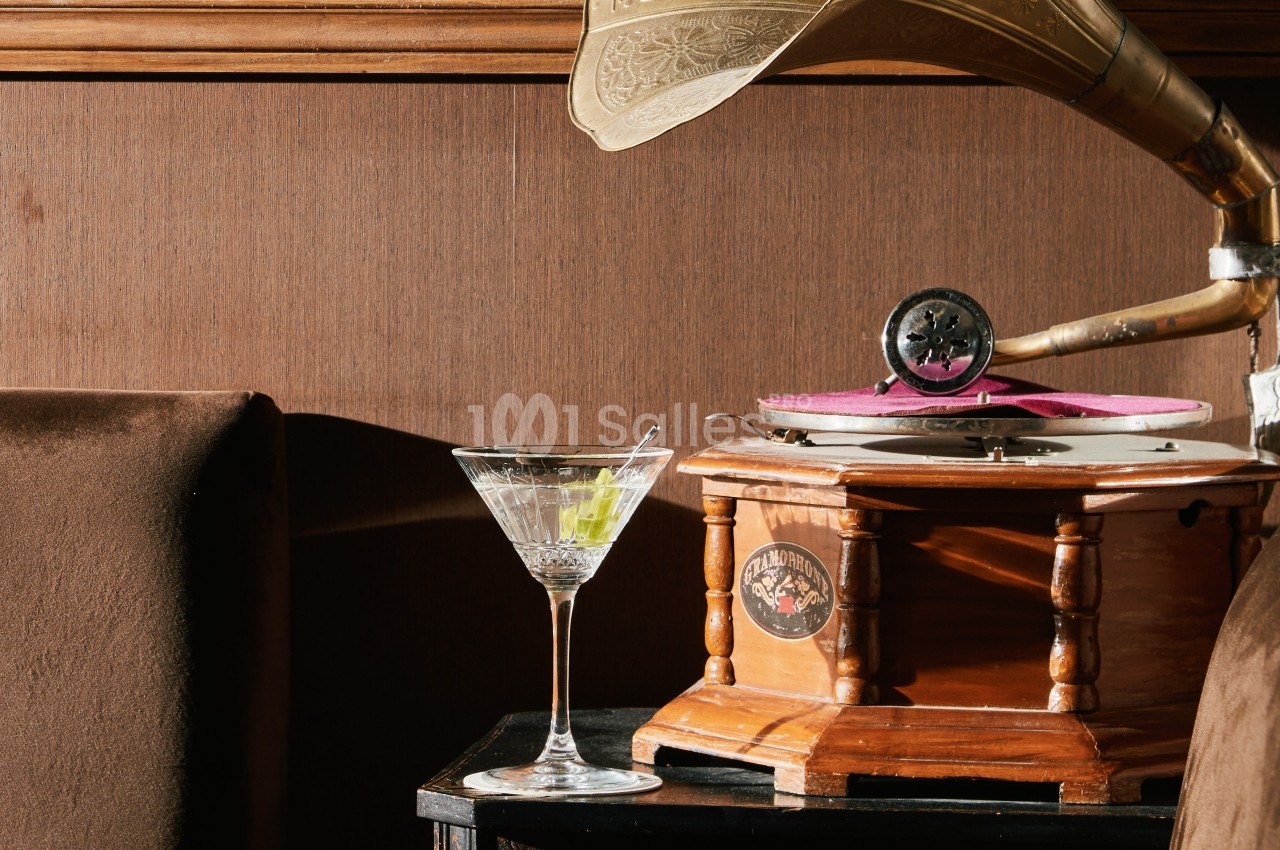 Un gramophone ancien en bois à côté d'un verre à cocktail sur une table sombre, dans un décor rétro.