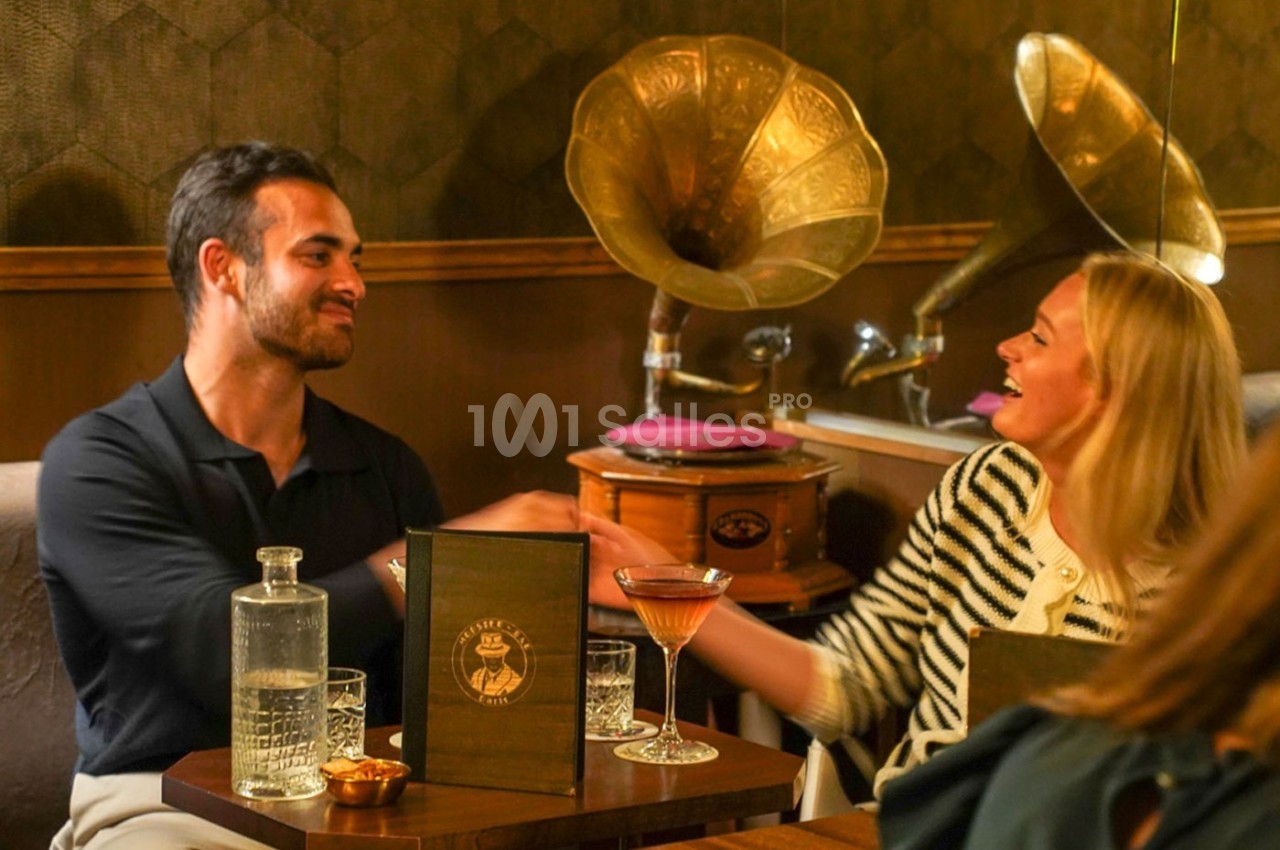 Un homme et une femme sourient et se serrent la main dans un café rétro avec des gramophones en arrière-plan.