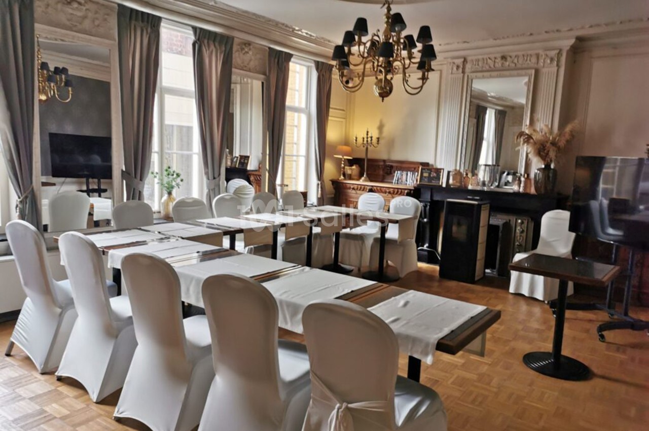 Salle élégante avec des tables disposées en U, chaises blanches, lustres et grandes fenêtres laissant entrer la lumière.
