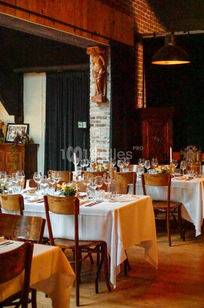 Salle de restaurant avec tables dressées, nappes blanches, verres et décorations, dans un cadre chaleureux en bois et…