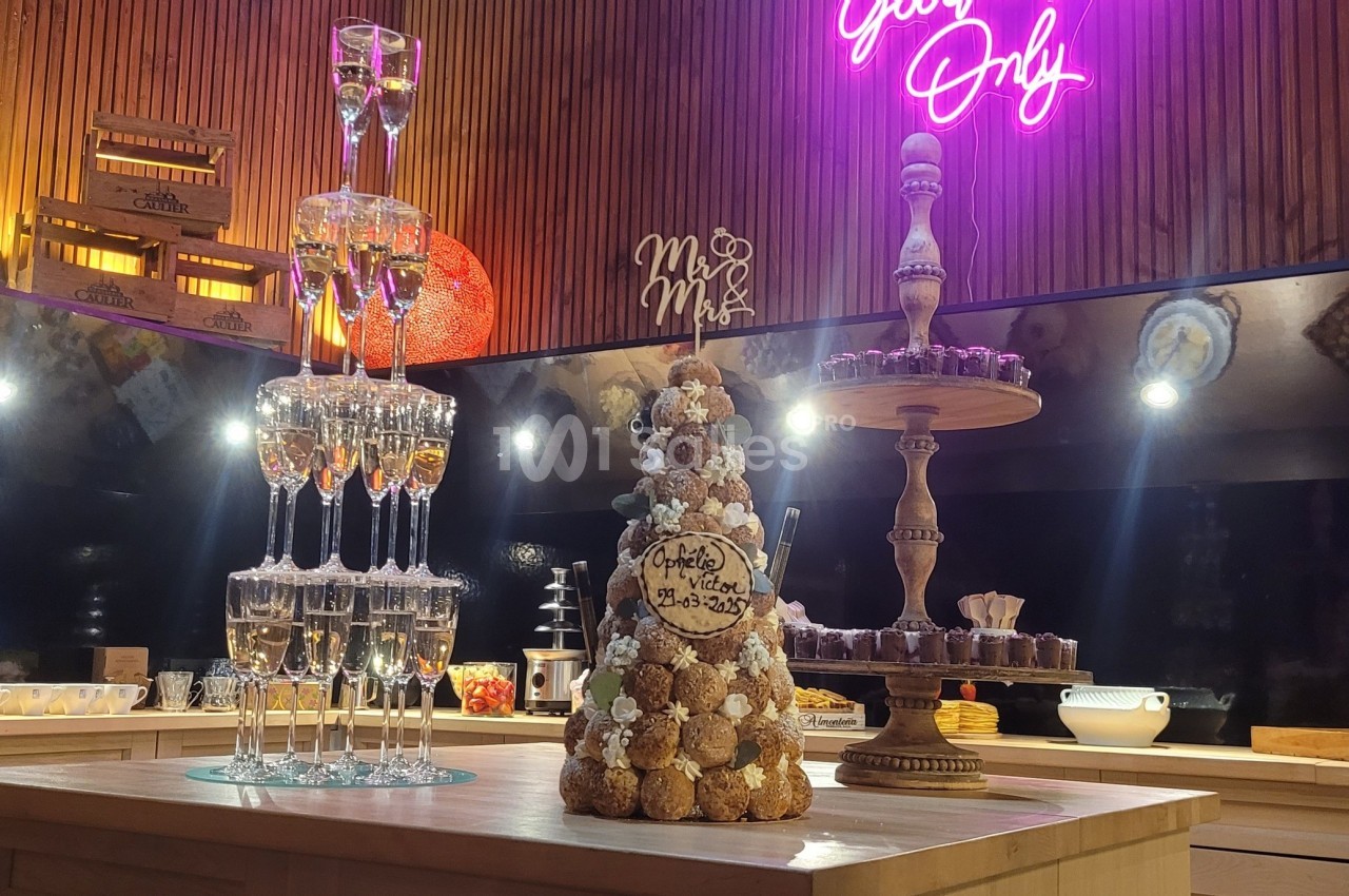 Tour de coupes de champagne et pièce montée en choux sur une table, dans une salle décorée avec éclairage néon.