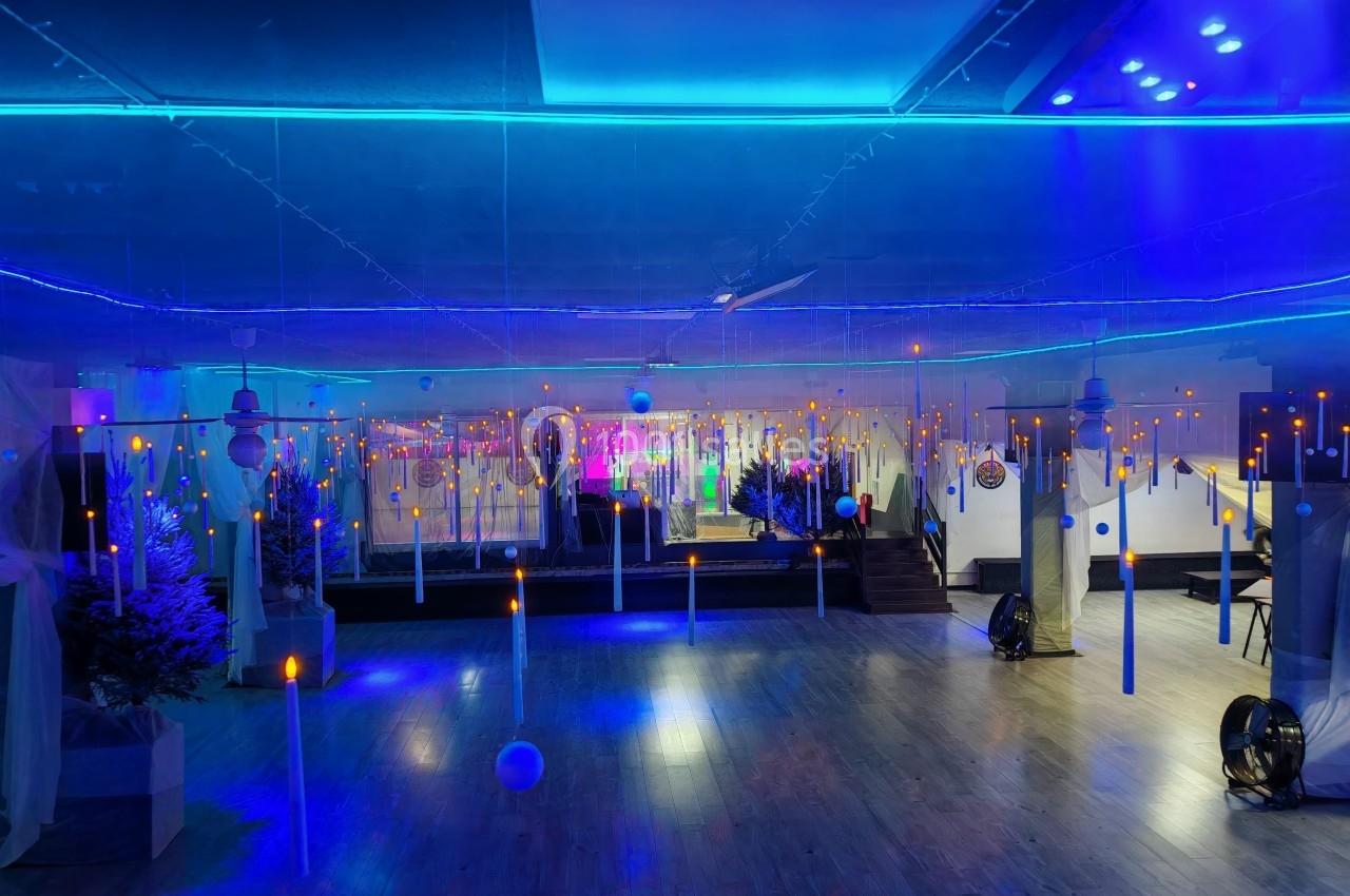 Salle décorée avec des lumières bleues et des bougies suspendues, ambiance immersive avec des sapins en arrière-plan.