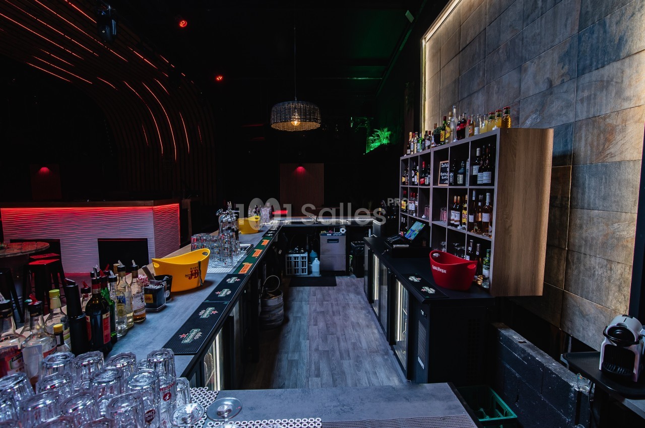Bar moderne avec comptoirs équipés de bouteilles, verres et accessoires, éclairage tamisé et ambiance chaleureuse.