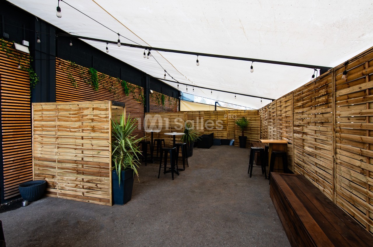 Terrasse extérieure couverte avec des cloisons en bois, des tables, des tabourets et des plantes en pot.