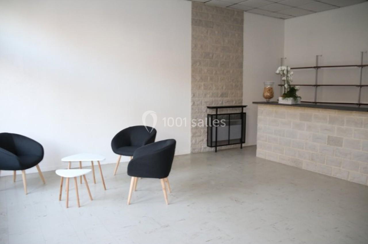 Espace intérieur minimaliste avec trois fauteuils noirs, tables basses blanches et un comptoir en pierre.