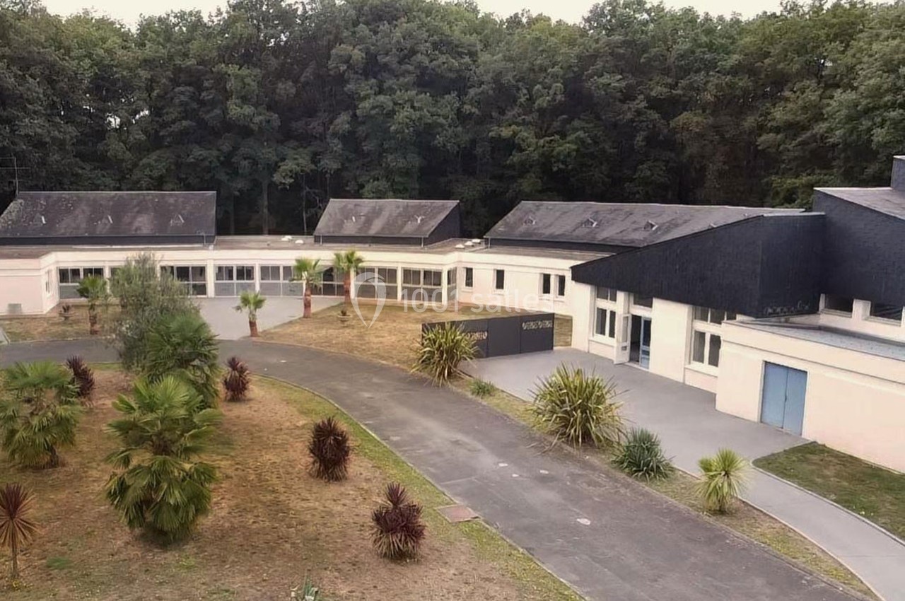 Bâtiment moderne entouré de végétation, avec une allée centrale et une forêt en arrière-plan.