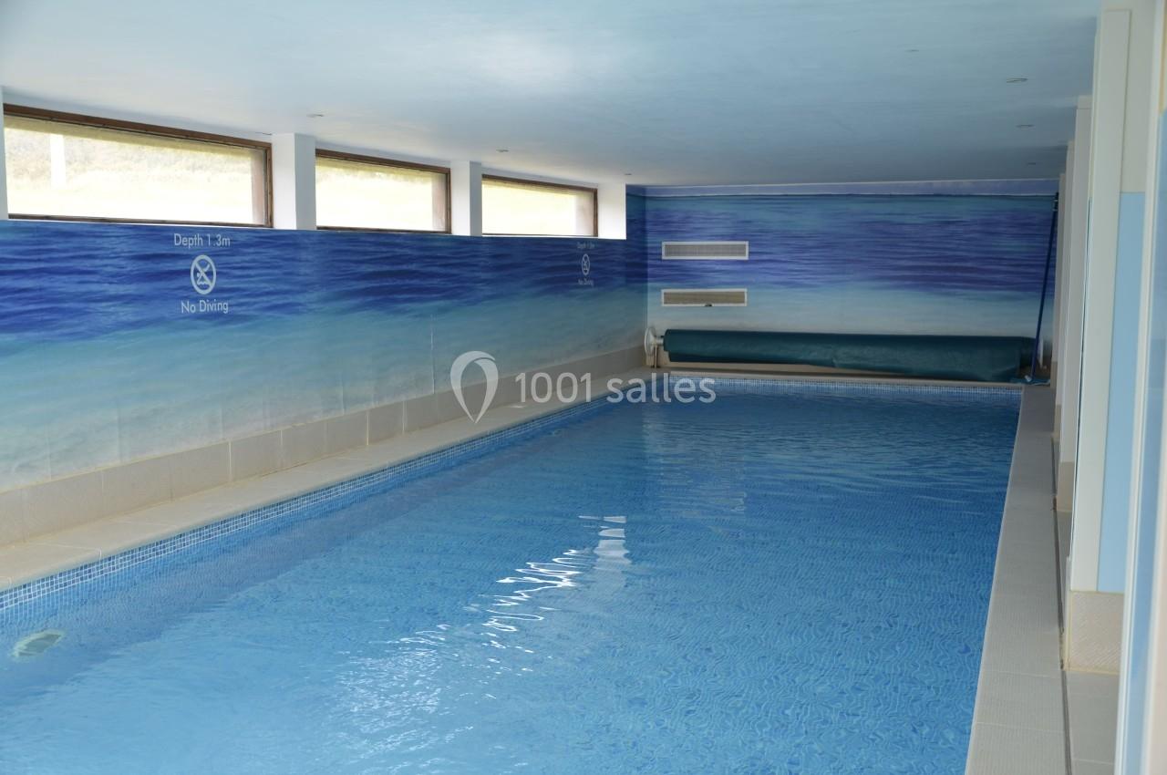 Piscine intérieure avec eau calme, murs peints en bleu et fenêtres laissant entrer la lumière naturelle.