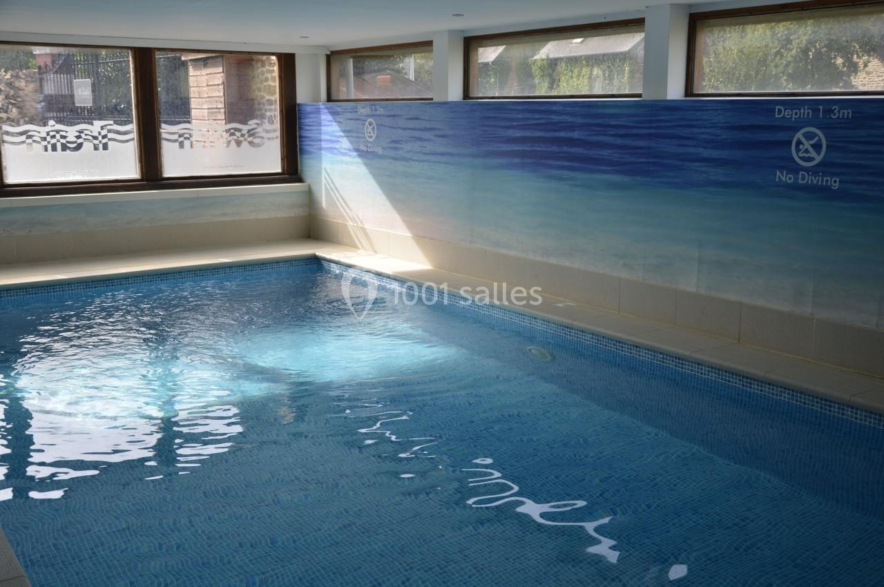 Piscine intérieure avec carrelage bleu, éclairée par des fenêtres laissant entrer la lumière naturelle.