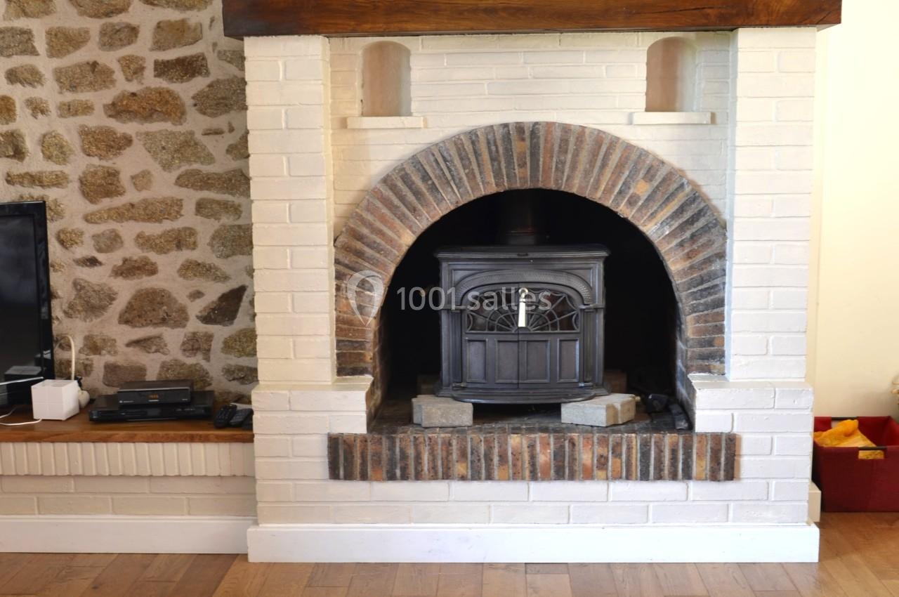 Poêle à bois noir encastré dans une cheminée en briques blanches et rouges, avec un mur en pierres apparentes à gauche.