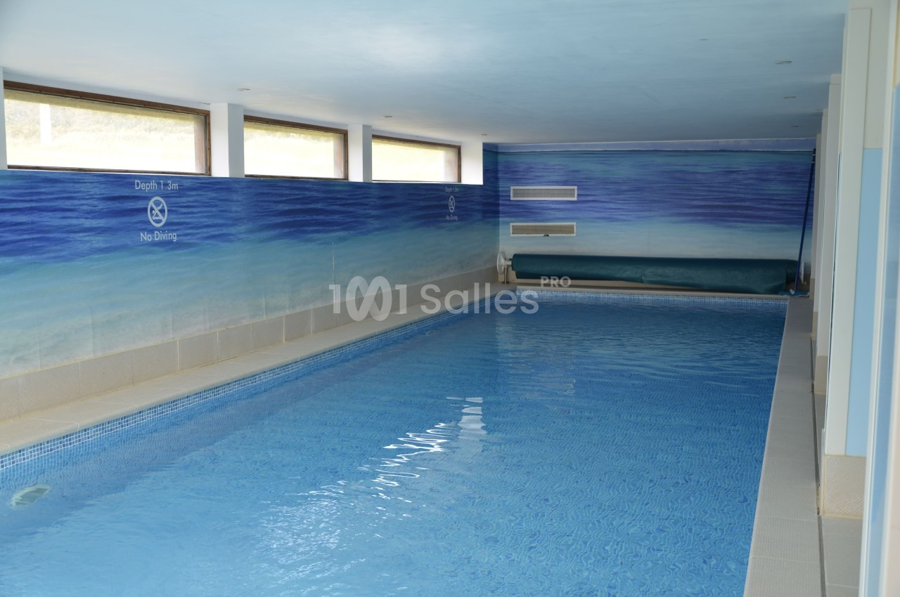 Piscine intérieure avec eau calme, murs peints en bleu et fenêtres laissant entrer la lumière naturelle.