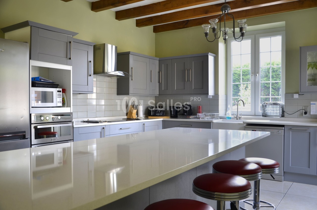 Cuisine moderne avec îlot central, meubles gris, électroménagers intégrés, et lumière naturelle entrant par une grande…