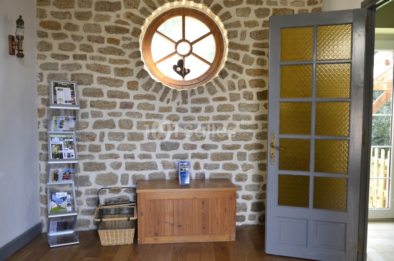 Mur en pierres apparentes avec une fenêtre ronde, une porte vitrée jaune, un banc en bois et un présentoir à brochures.