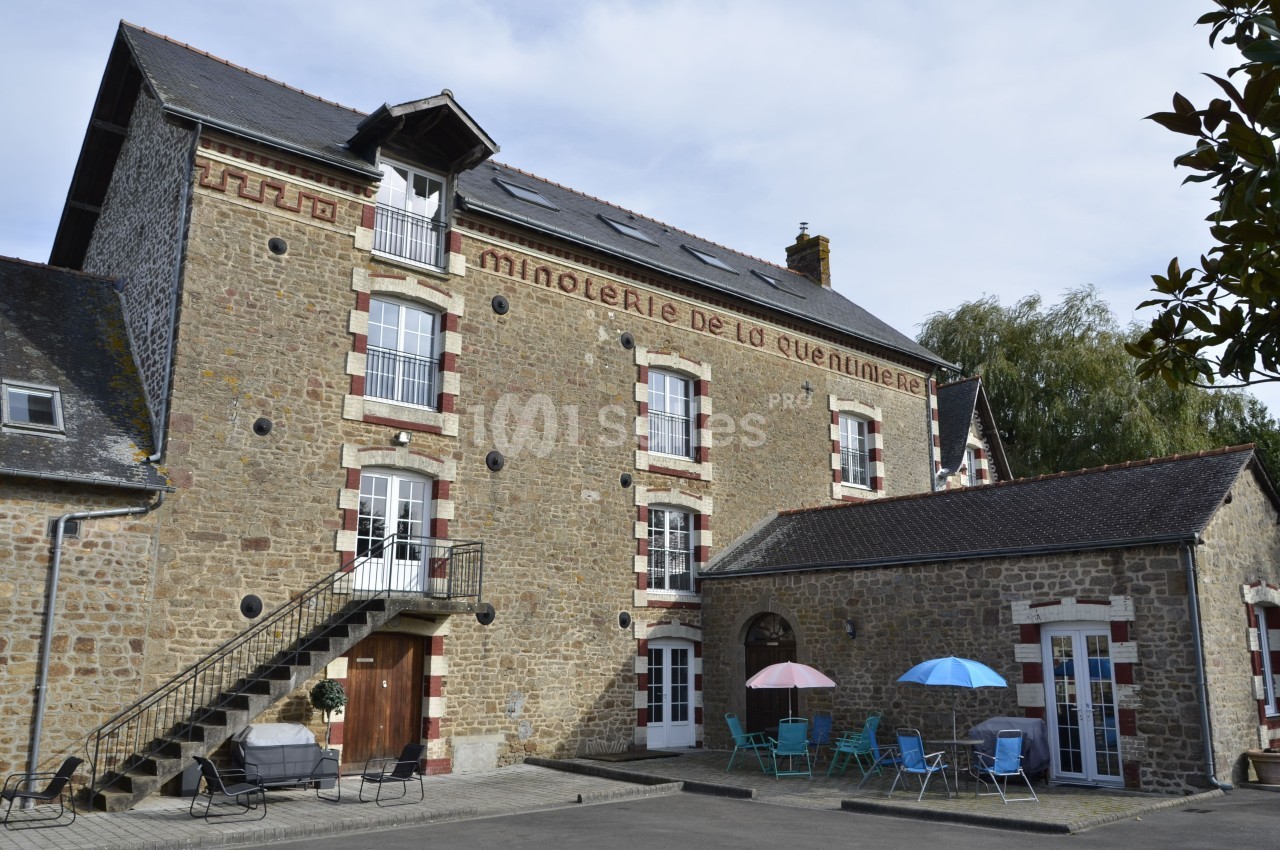 Bâtiment en pierre avec des fenêtres rouges et blanches, terrasse équipée de tables et parasols colorés.
