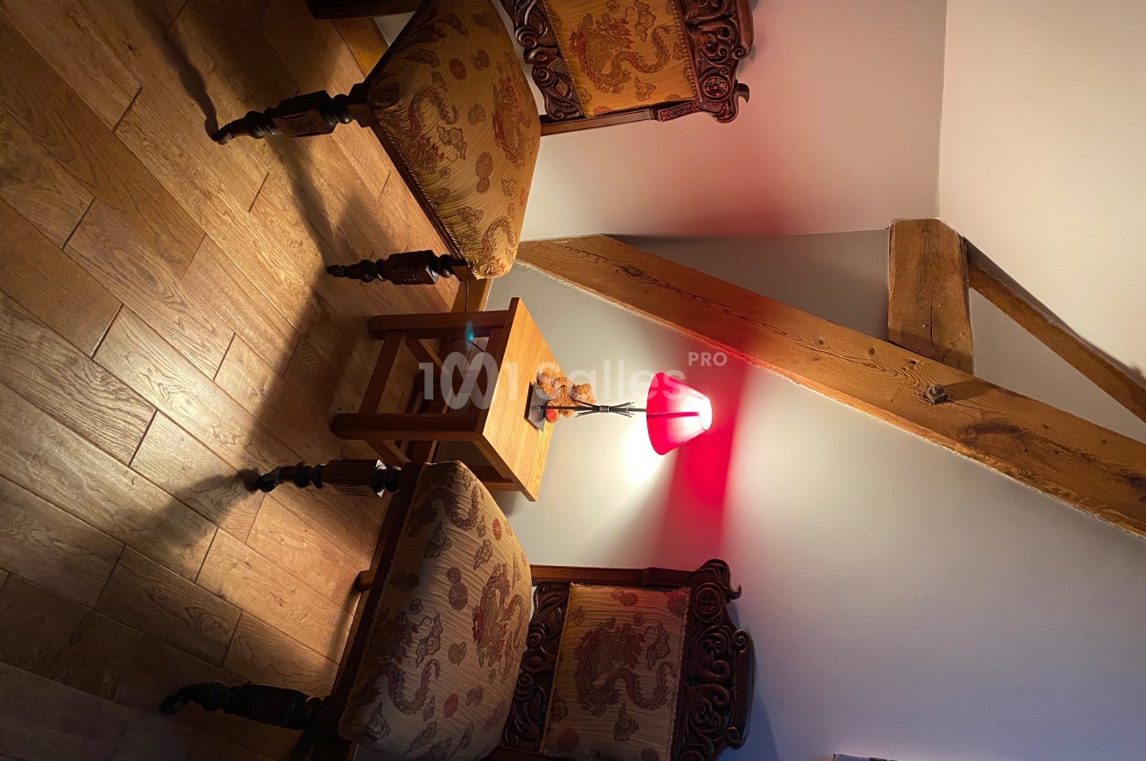 Deux chaises en bois sculpté avec assises rembourrées entourent une petite table éclairée par une lampe rouge.