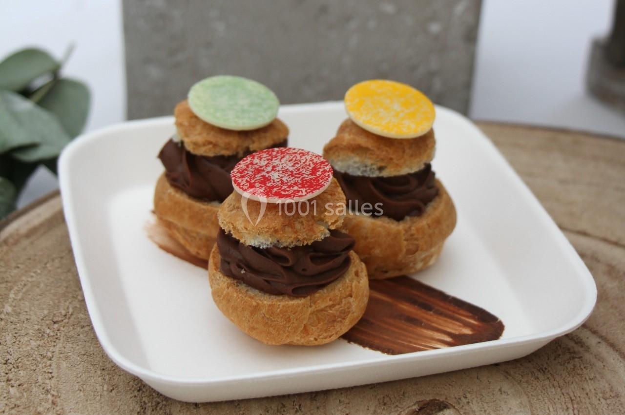 Assortiment de choux garnis de crème au chocolat, décorés de disques colorés, présentés sur une assiette blanche.