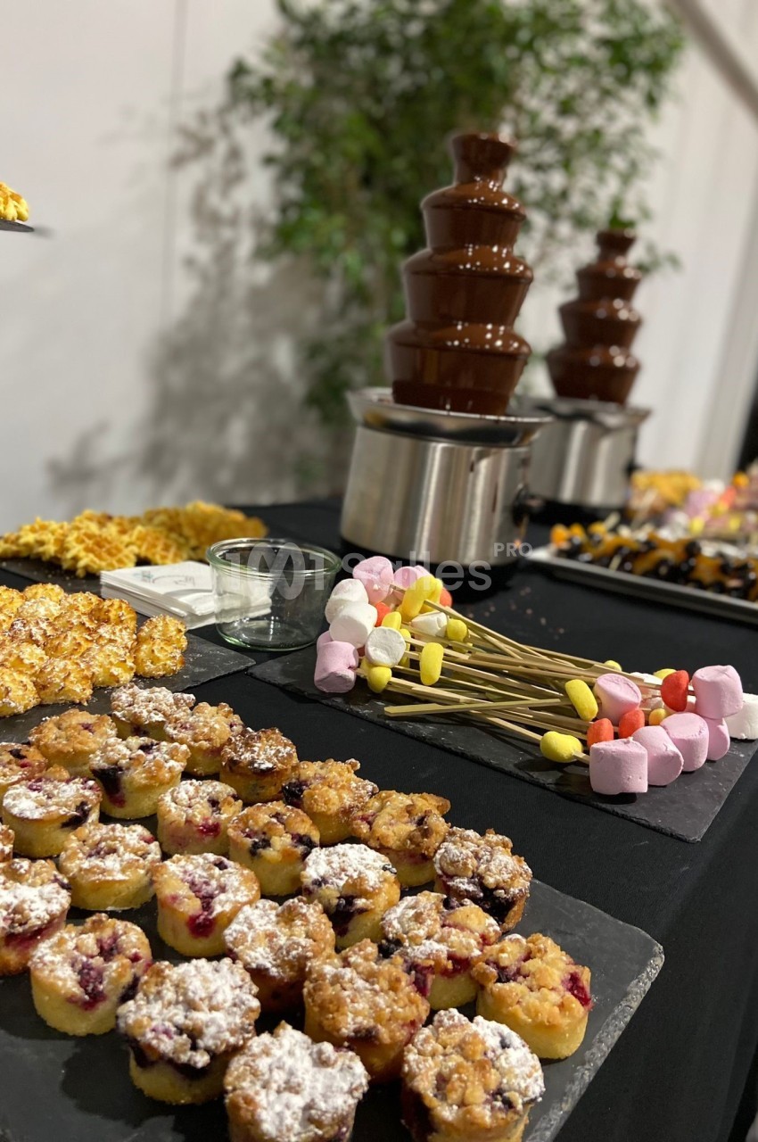 Table avec fontaine à chocolat, brochettes de guimauves, mini-gâteaux et pop-corn disposés pour un buffet dessert.
