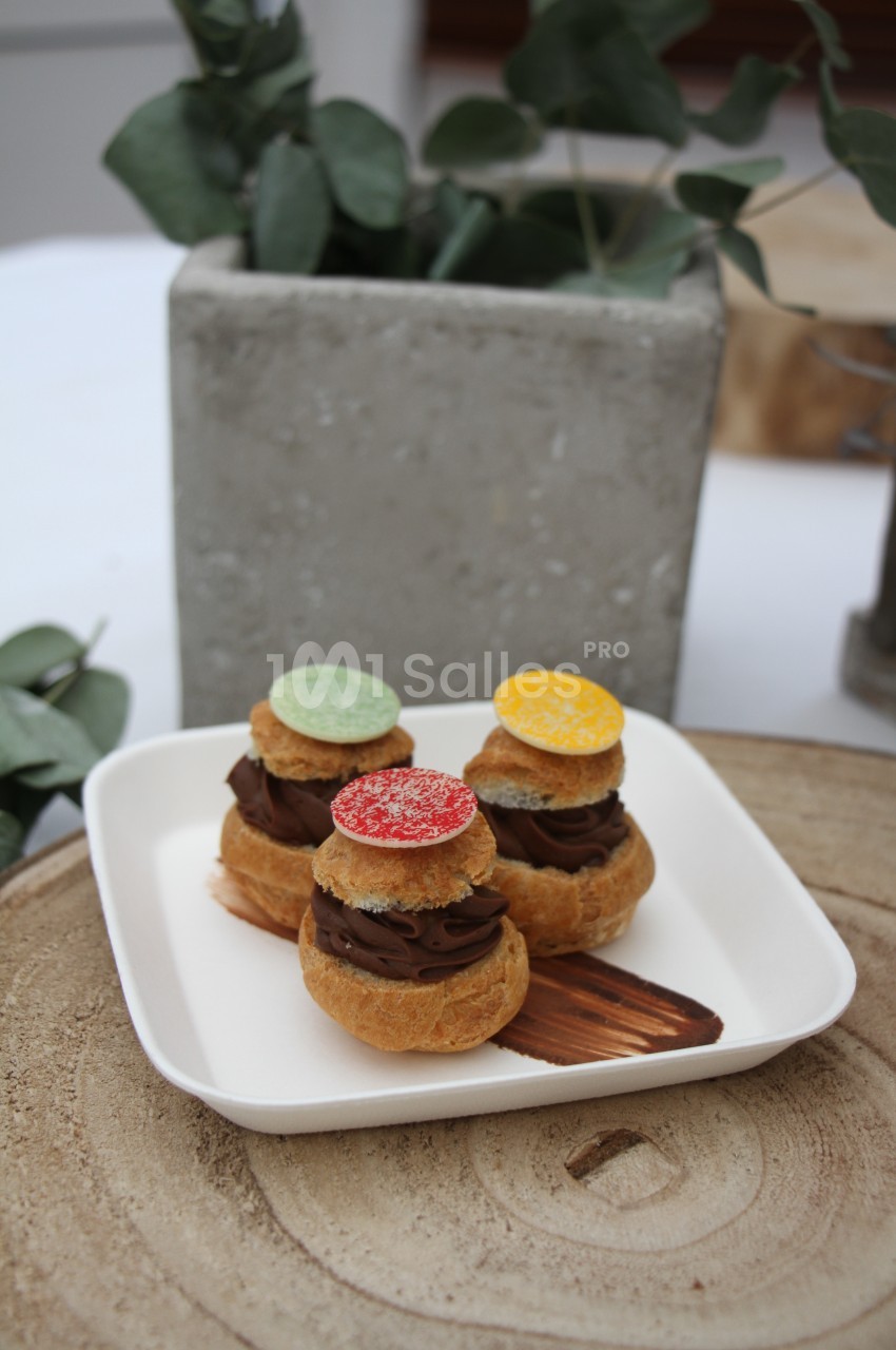 Assortiment de choux garnis de crème au chocolat, décorés de disques colorés, présentés sur une assiette blanche.