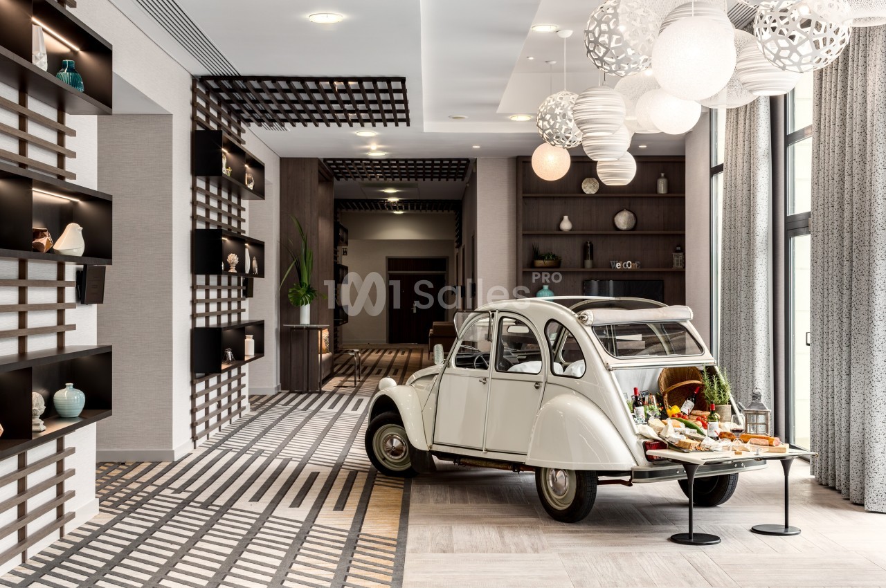 Une voiture ancienne blanche exposée dans un intérieur moderne, utilisée comme support pour un buffet décoratif.