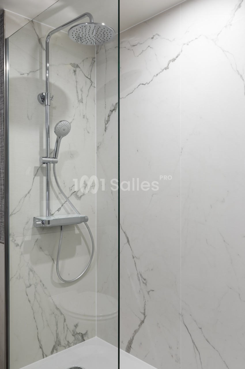 Douche moderne avec paroi en verre, pommeau fixe et mobile, sur fond de carrelage effet marbre blanc.