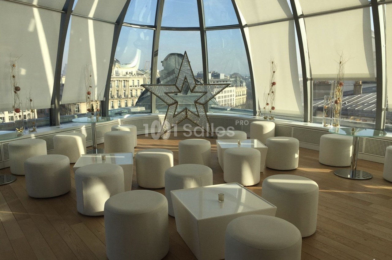 Salle lumineuse avec de grandes baies vitrées, mobilier blanc moderne et une étoile décorative au centre.