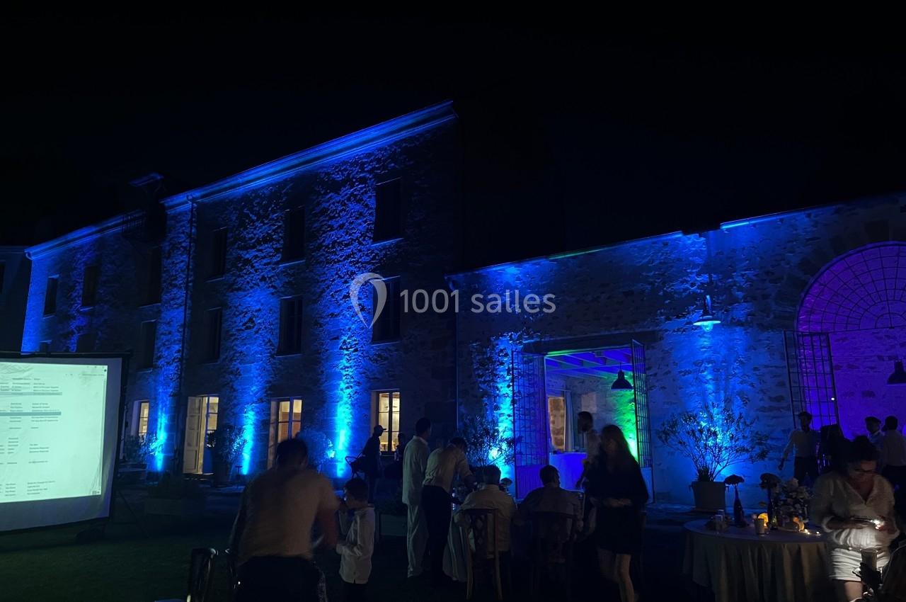 Façade d'un bâtiment en pierre éclairée par des lumières colorées lors d'un événement nocturne en extérieur.